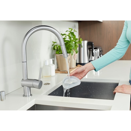 Foto van een persoon die de BLACK+DECKER DVA325JP07 afspoelt met water in een moderne gootsteen, zijaanzicht.