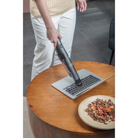 BLACKDECKER DVC320B21 handstofzuiger reinigt laptoptoetsenbord op houten tafel, zijaanzicht