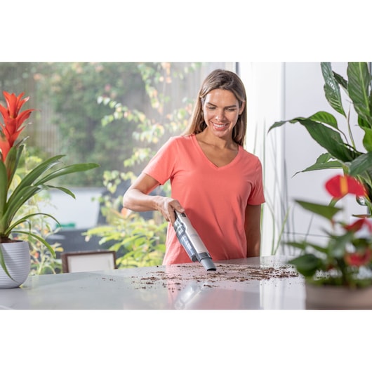 BLACKDECKER DVC320BRG handstofzuiger verwijdert vuil van een witte tafel met kamerplanten.