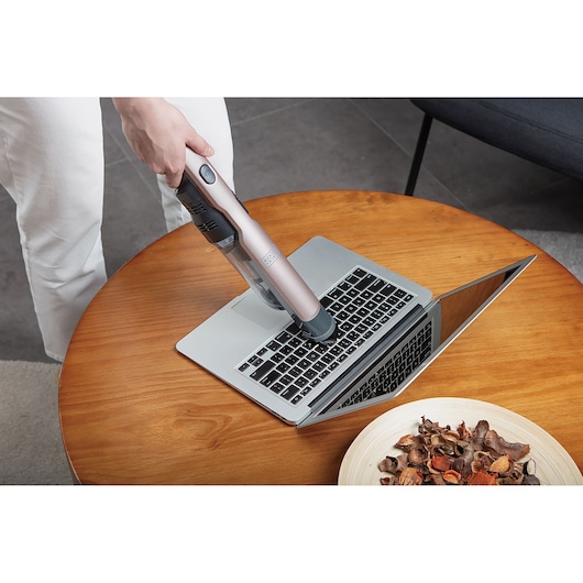 BLACK+DECKER DVC320BRG handstofzuiger reinigt laptoptoetsenbord op houten tafel.