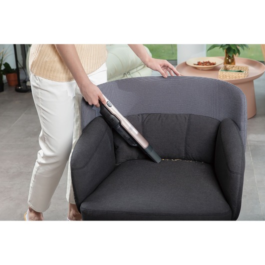BLACKDECKER DVC320BRG handstofzuiger verwijdert kruimels van een donkere fauteuil in de woonkamer.