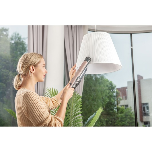 BLACK+DECKER DVC320BRG handstofzuiger wordt gebruikt om een witte lampenkap te reinigen in een moderne woonkamer.