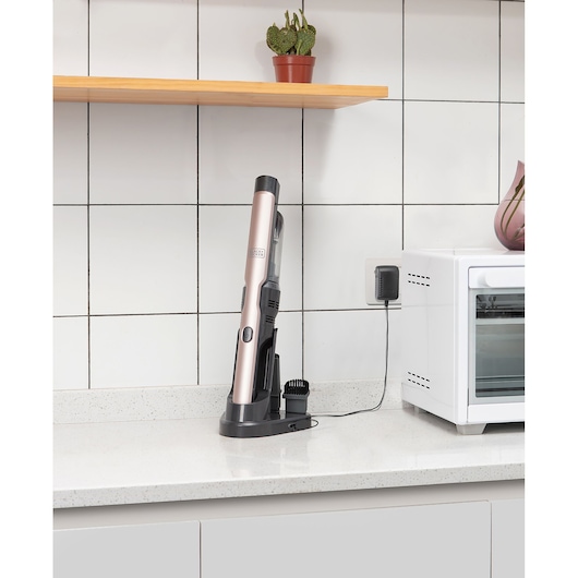BLACKDECKER DVC320BRG handstofzuiger in roségoud aan het opladen op een aanrecht naast een witte oven.