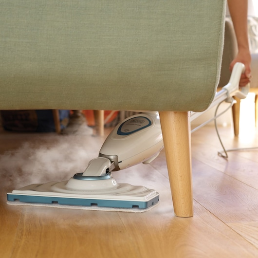 BLACKDECKER FSM1605 balai vapeur nettoyant le sol en bois sous le canapé, vue rapprochée.