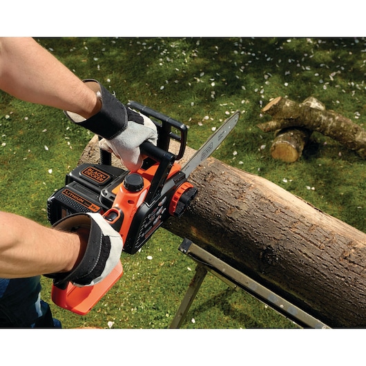 BLACK+DECKER GKC3630L25 snoerloze kettingzaag zaagt buiten een houtblok, gebruiker draagt handschoenen.