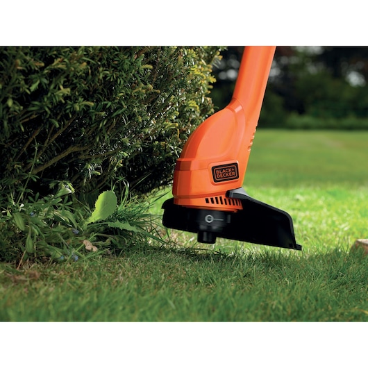 BLACK+DECKER GL250 coupe-bordures orange utilisé près des arbustes sur une pelouse.