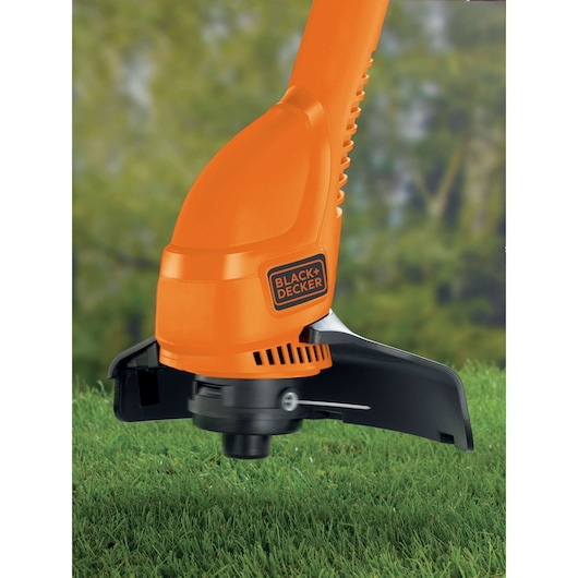 Gros plan sur la tête de coupe du BLACK+DECKER GL310 orange sur la pelouse en extérieur.