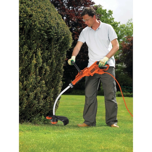 BLACKDECKER GL7033CAKIT oranje elektrische grastrimmer in gebruik buiten op gazon bij struiken.