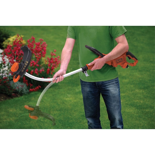 BLACK+DECKER GL7033CAKIT oranje-zwarte grastrimmer, in gebruik op een groen gazon met tuin op de achtergrond.