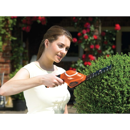Foto van BLACK+DECKER GSL700 snoerloze struikschaar in gebruik bij het snoeien van een struik in de tuin.