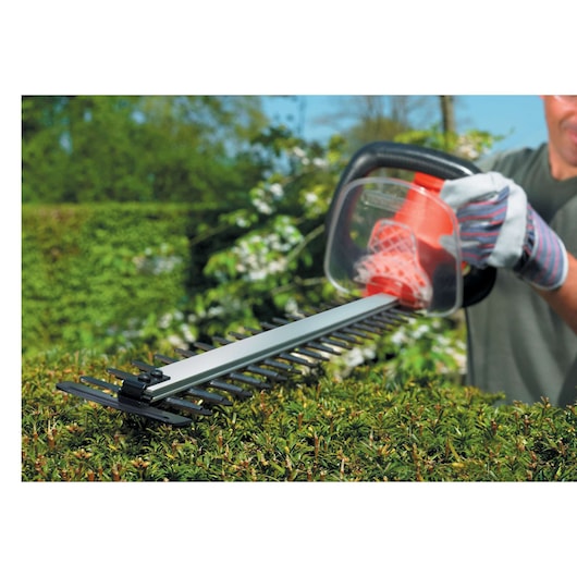 Foto van de BLACKDECKER GT7030 heggenschaar in gebruik, snoeit groen struikgewas buiten.