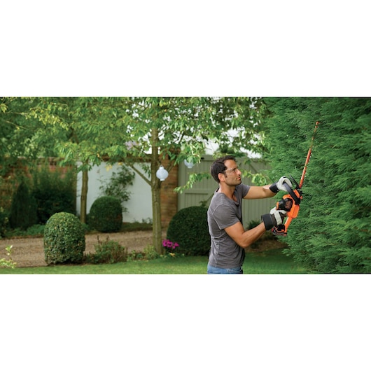 Foto van persoon die met BLACK+DECKER GTC18452PCB snoerloze heggenschaar een groene heg in de tuin snoeit.
