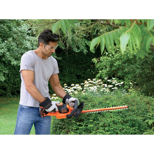 Foto van persoon die struiken snoeit met BLACK+DECKER heggenschaar GTC18452PCB in een tuin.