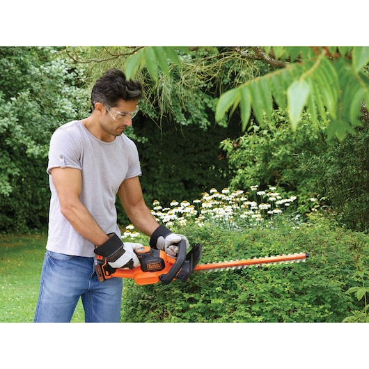 Foto van persoon die de BLACK+DECKER GTC18452PC heggenschaar gebruikt en groene struiken snoeit in de tuin.