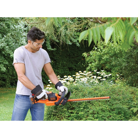 BLACKDECKER GTC18504PC heggenschaar gebruikt op struiken buiten, oranje en zwart, draadloos.
