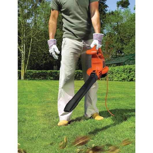 BLACKDECKER GW3030 elektrische bladblazer in gebruik op gras, persoon met handschoenen houdt het oranje gereedschap vast.