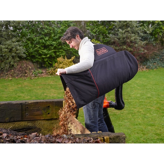 Foto van BLACKDECKER GWBP1 tuinbladerenverzamelzak die bladeren leegt naast een houten compostbak.