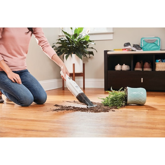 BLACKDECKER HLVC315B11 handheld stofzuiger verwijdert aarde van omgevallen plant op houten vloer, binnenruimte.