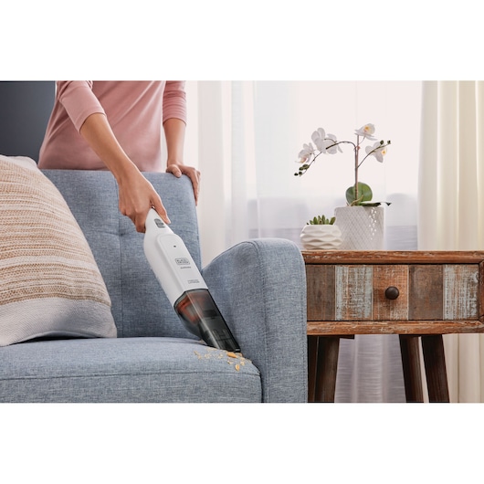 BLACK+DECKER HLVC315B11 handstofzuiger verwijdert kruimels van blauwe bank naast houten bijzettafel.
