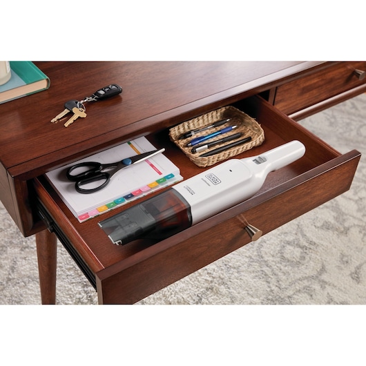 BLACK+DECKER HLVC315B11 handstofzuiger in een houten bureaulade met schaar, notitieblok en pennen.