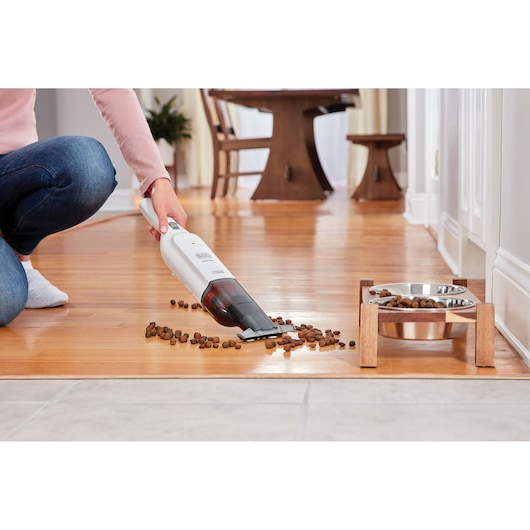 BLACKDECKER HLVC315J11 handstofzuiger schoonmaakt dierenvoer op houten vloer bij voerbakken.