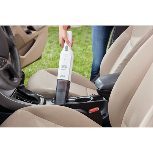 BLACKDECKER HLVC315J11 handstofzuiger reinigt het interieur van een auto tussen beige stoelen.