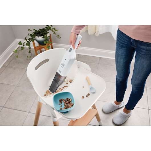 BLACKDECKER HLVC315J11 handstofzuiger zuigt gemorst ontbijtgranen op een kinderstoelblad, binnenomgeving.