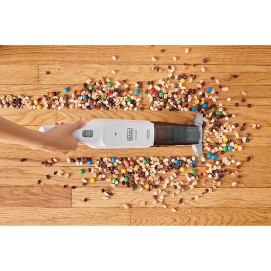 Foto van BLACKDECKER HLVC315J11 handstofzuiger die gemengde snacks van houten vloer schoonmaakt.