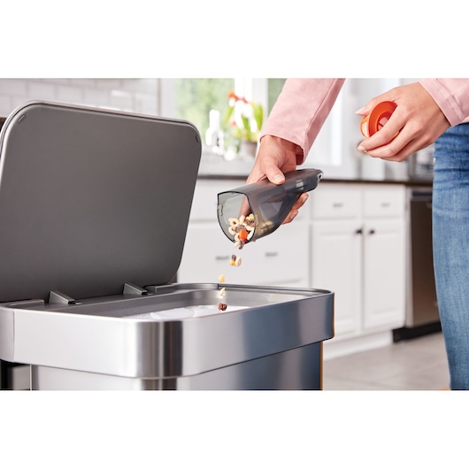 BLACKDECKER HLVC315J11 handstofzuiger stofbak wordt geleegd in een keukenprullenbak.
