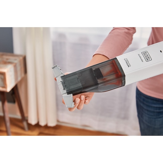 Foto van BLACK+DECKER HLVC315J11 draadloze handstofzuiger die wordt geleegd, vastgehouden door een persoon binnen.