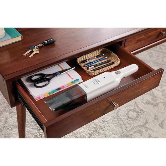 Foto van BLACKDECKER HLVC315J11 handstofzuiger in een houten bureaulade met kantoorspullen.