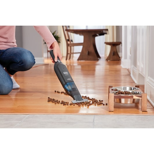 BLACKDECKER HLVC320B11 handstofzuiger verwijdert dierenvoer op houten vloer bij hondenbakken.