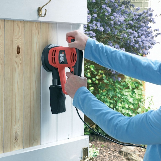 BLACKDECKER KA191EK schuurmachine in gebruik op een houten deurpaneel buiten.