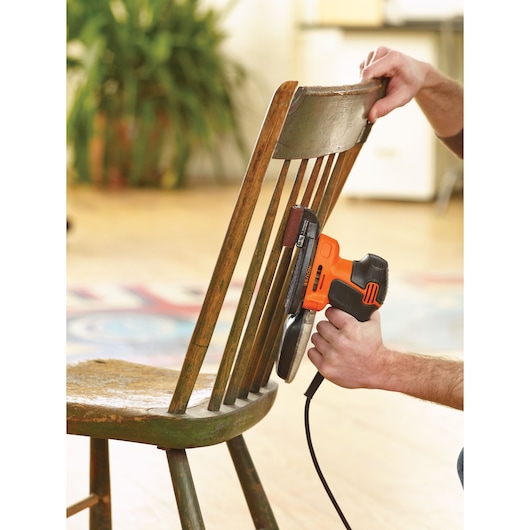 BLACKDECKER KA2000 ponceuse électrique ponçant les barreaux d'une chaise en bois en intérieur.
