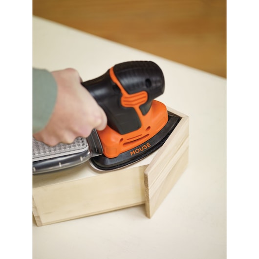 BLACKDECKER KA2000 ponceuse mouse orange et noire en utilisation sur boîte en bois, vue rapprochée