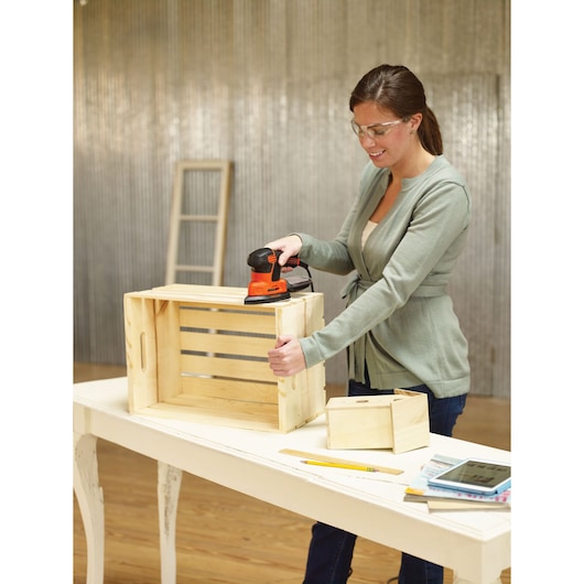 BLACKDECKER KA2000 ponceuse utilisée sur une caisse en bois dans un atelier, outils et livres sur table blanche.