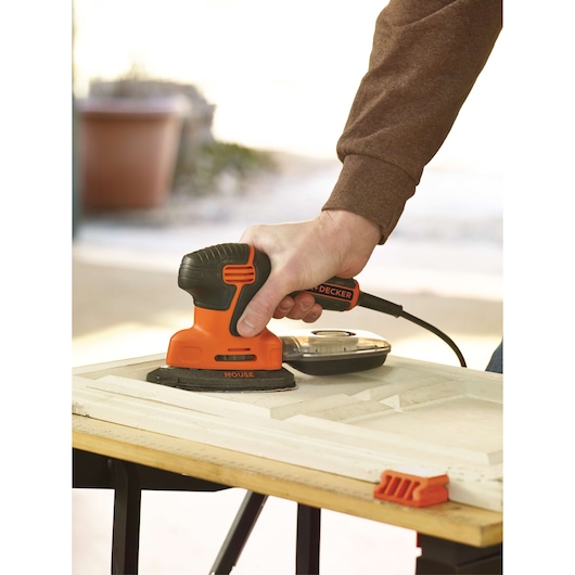 Personne ponçant du bois avec la ponceuse de détail orange et noire BLACKDECKER KA2000, vue rapprochée.