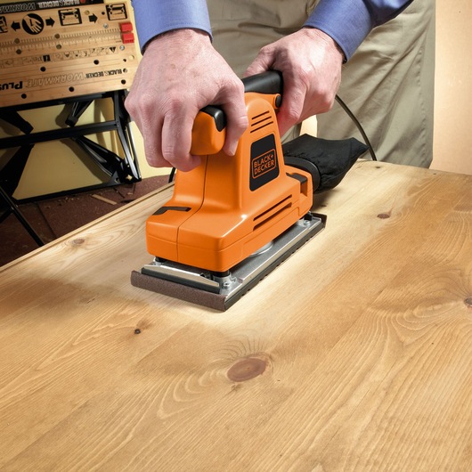 Foto van de oranje BLACK+DECKER KA274EKA vlakschuurmachine in gebruik op een houten oppervlak.