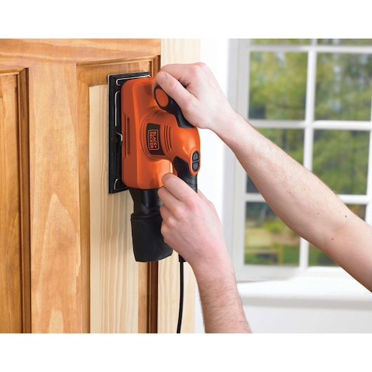 Foto van BLACKDECKER KA274EKA elektrische schuurmachine in gebruik op een houten deur in een huiselijke omgeving.