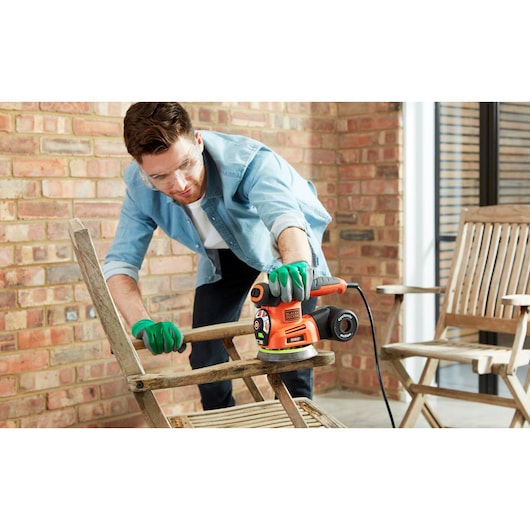 BLACKDECKER KA280LSA2 multischuurmachine in gebruik om een houten stoel te schuren, vastgehouden met handschoenen.
