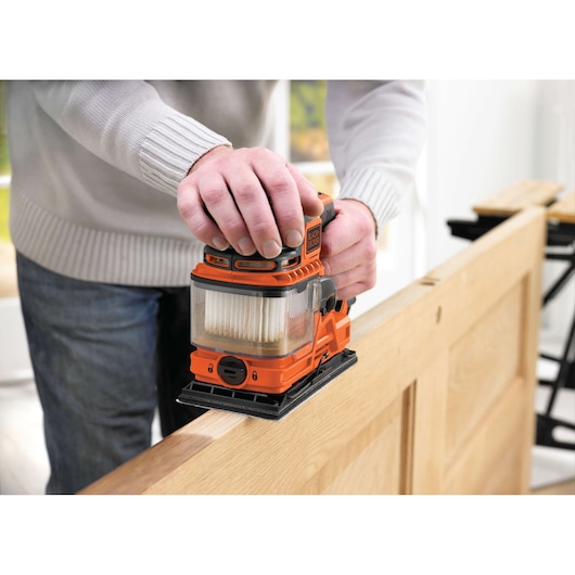 Foto van de oranje BLACK+DECKER KA330E schaafmachine in gebruik op een houten deur, close-up.