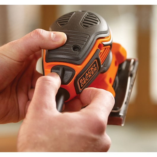 Close-up foto van BLACK+DECKER KA450 detailschuurmachine in gebruik met hand, oranje en zwarte behuizing zichtbaar.