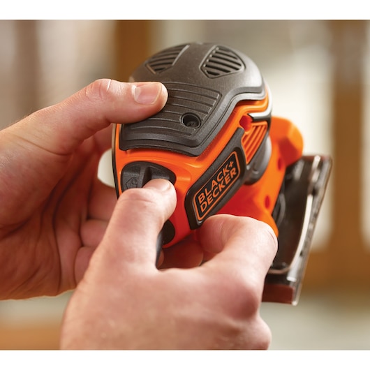 Close-upfoto van BLACK+DECKER KA450 schuurmachine in handen, compact zwart-oranje ontwerp.