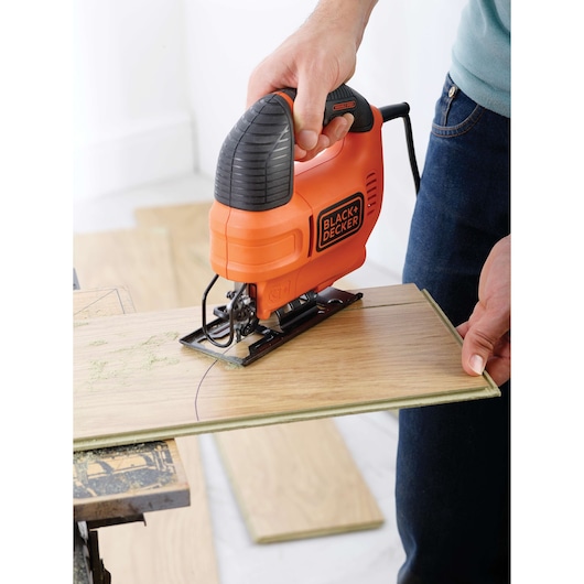 Foto van BLACKDECKER KS701EK decoupeerzaag die een houten paneel snijdt, ergonomisch oranje-zwart ontwerp.