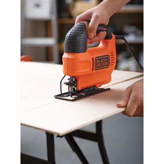 BLACKDECKER KS701EK oranje decoupeerzaag in gebruik om hout te zagen op een werkbank, close-up fotografie.