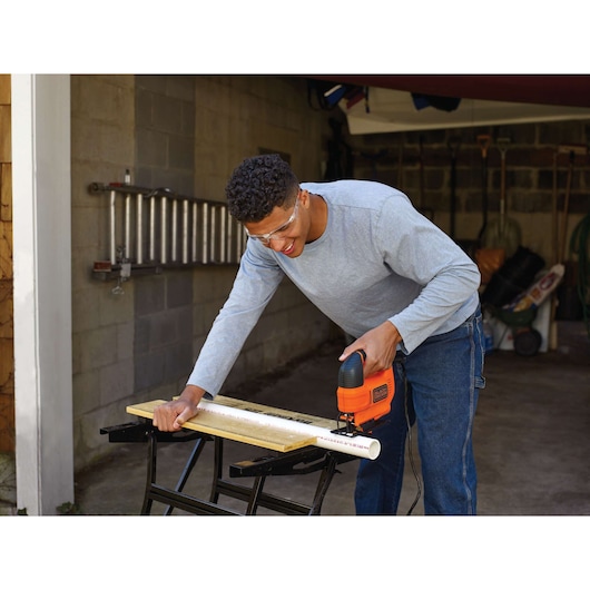 BLACKDECKER KS701E decoupeerzaag snijdt PVC-buis op werkbank in een garage.