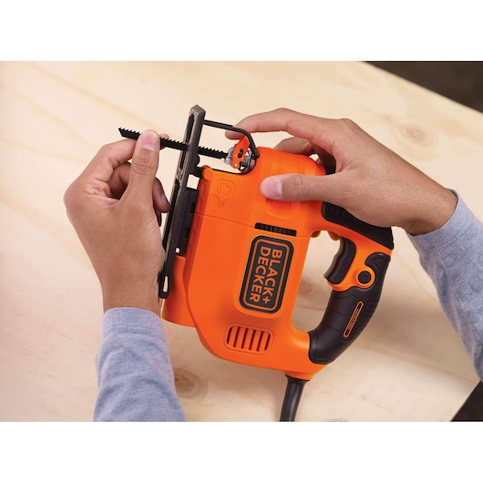 Foto van BLACK+DECKER KS701PEK decoupeerzaag in gebruik, oranje behuizing met zwarte accenten, zaagblad zichtbaar, op hout.