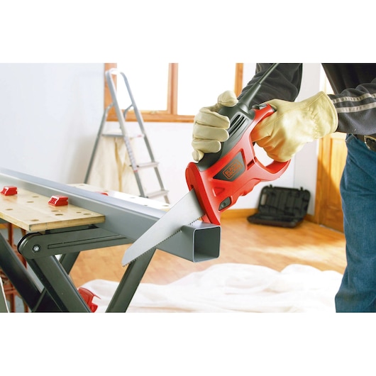 BLACKDECKER KS880EC scie électrique coupant un tube métallique, personne avec des gants, atelier intérieur.