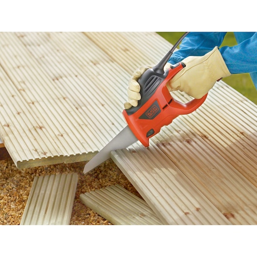 BLACKDECKER KS880EC scie électrique coupant des planches en bois, gros plan main gantée en extérieur.