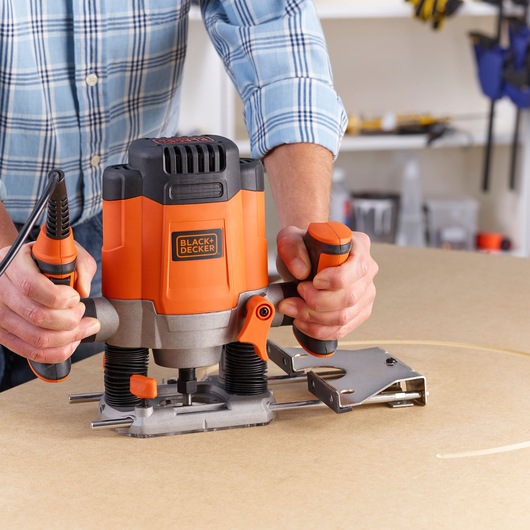 Photo de la défonceuse plongeante BLACK+DECKER KW1200EKA utilisée sur du bois, vue rapprochée, utilisateur tenant les poignées.